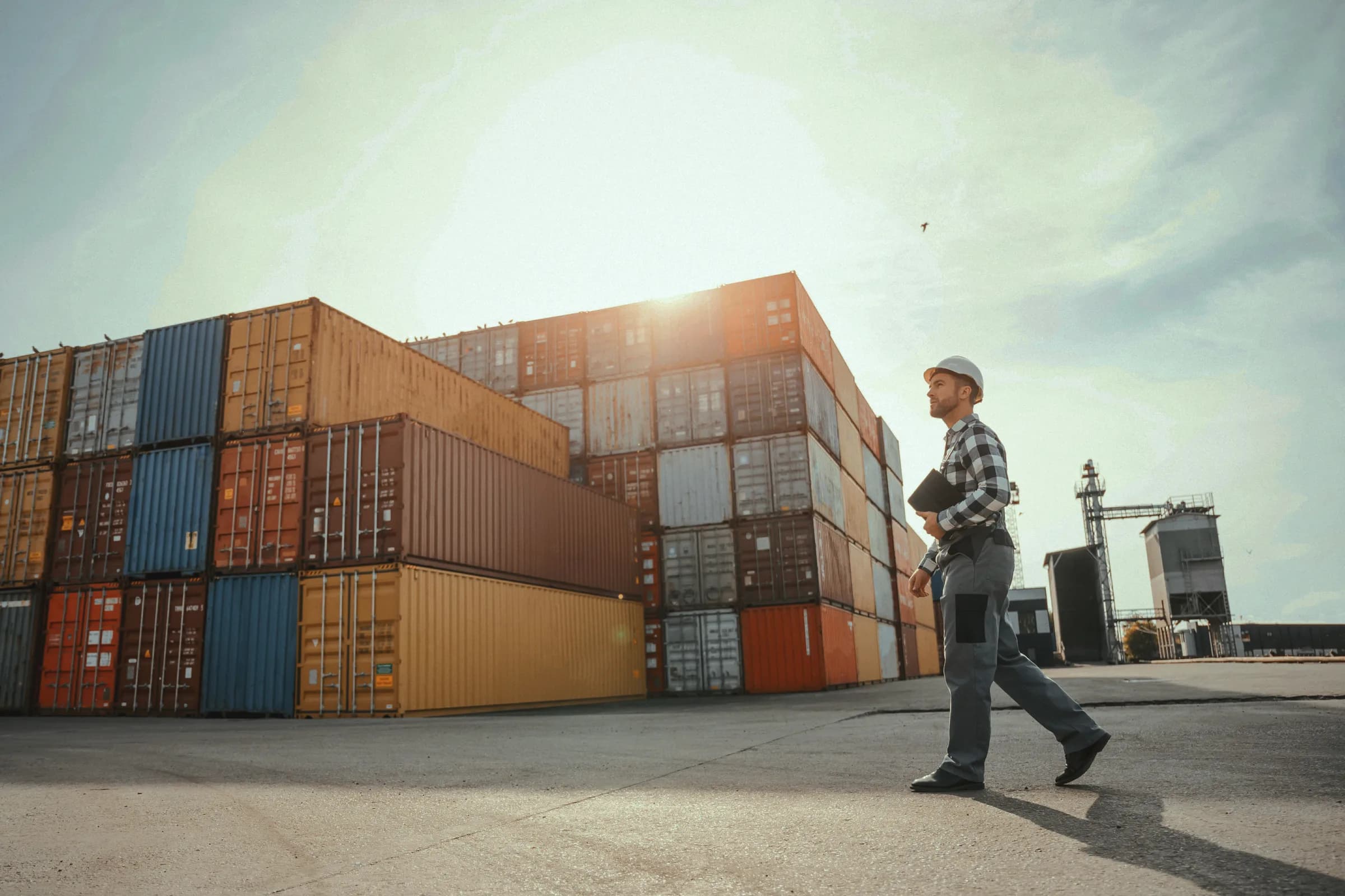 Stacked shipping containers at a port with a logistics worker reviewing operations