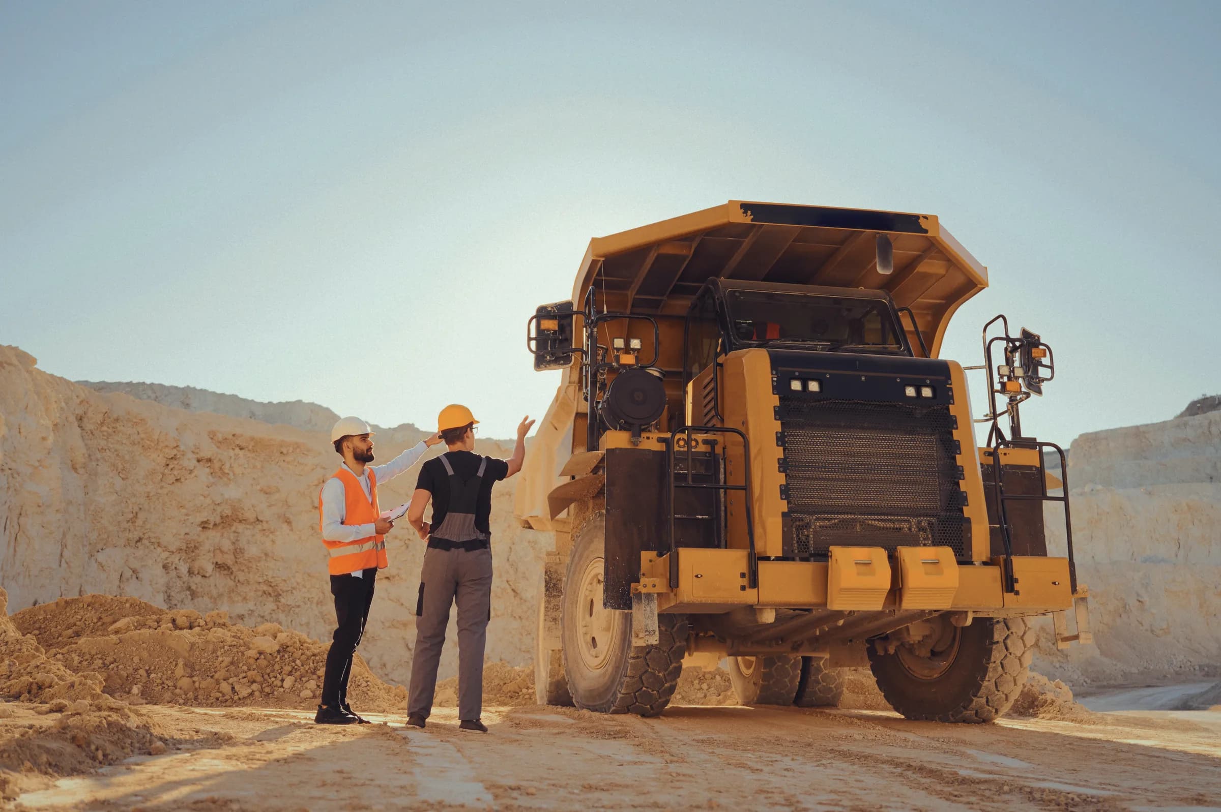 Two mining workers beside a large haul truck at an open-pit site